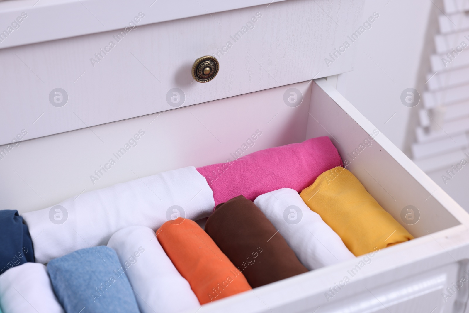 Photo of Open drawer with rolled shirts indoors. Organizing clothes