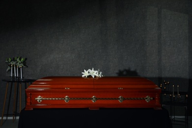 Photo of Wooden casket with white lilies and burning candles in funeral home