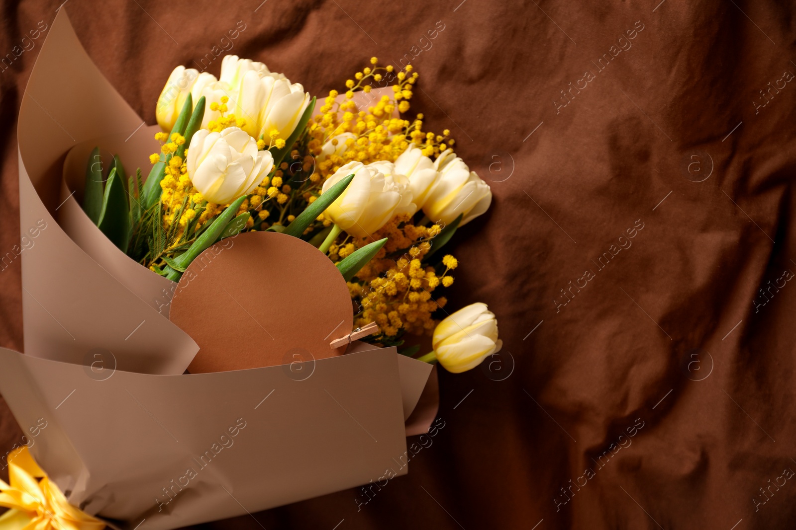 Photo of Bouquet of beautiful spring flowers and blank card on brown fabric, top view. Space for text