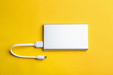 Photo of Modern portable charger with cable on yellow background, top view
