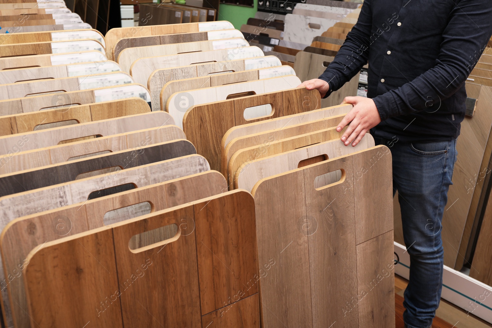 Photo of Man choosing wooden flooring among different samples in shop, closeup