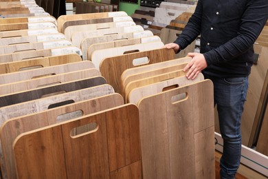 Photo of Man choosing wooden flooring among different samples in shop, closeup