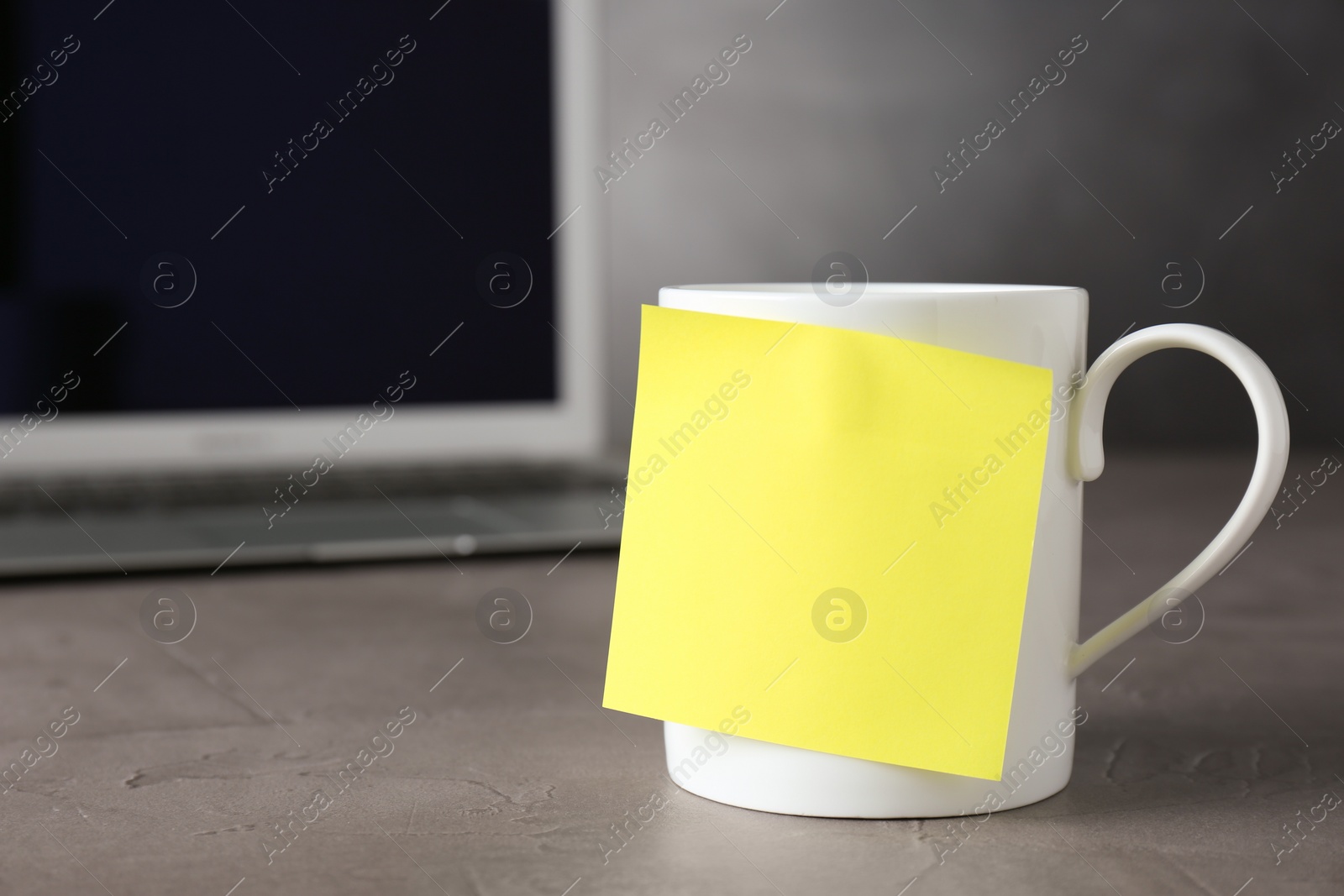 Photo of Cup with blank sticky note on grey table. Space for text