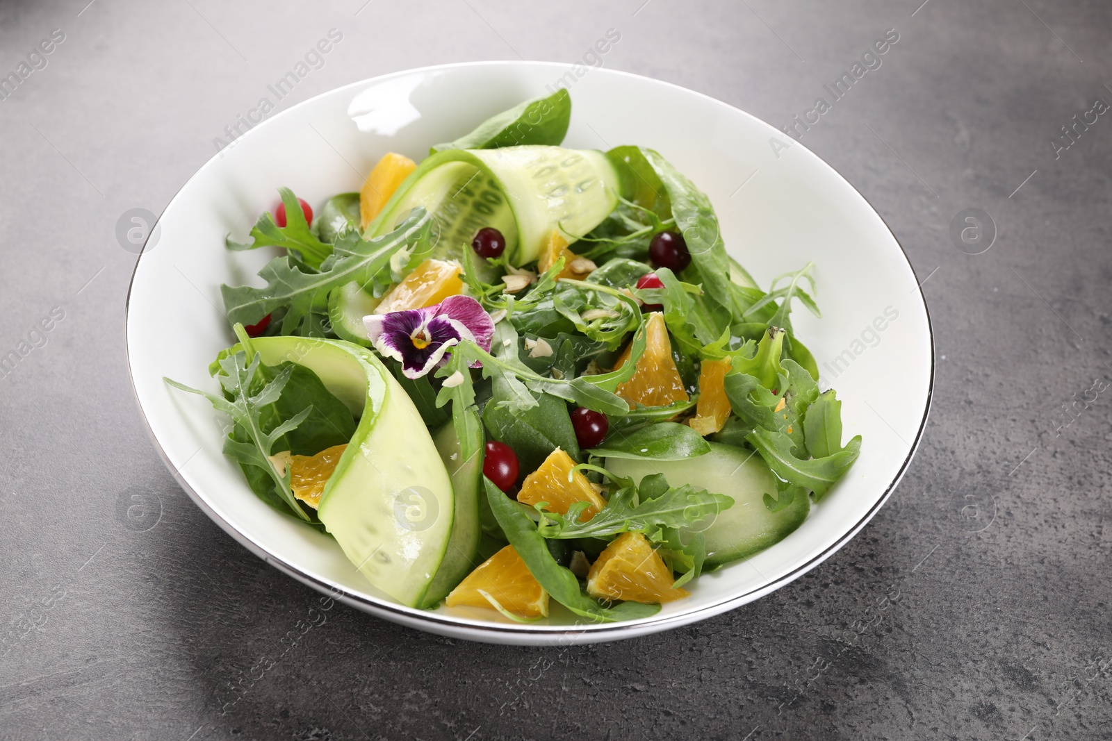 Photo of Delicious salad with cucumber and orange slices on gray table