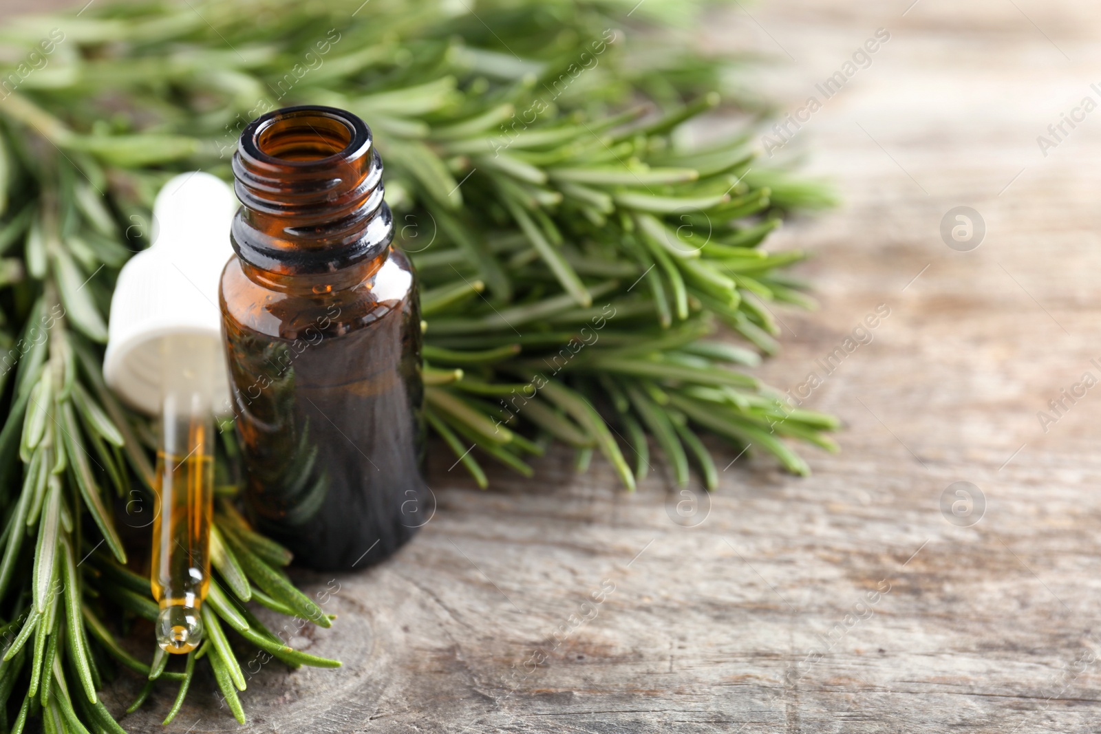 Photo of Bottle of rosemary essential oil on wooden background