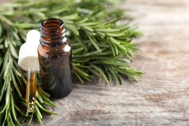 Photo of Bottle of rosemary essential oil on wooden background