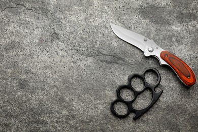 Photo of Brass knuckles and knife on grey background, flat lay. Space for text