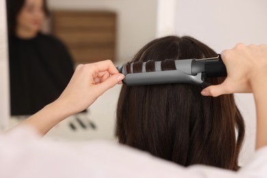 Hairdresser working with client using curling hair iron in salon, closeup