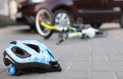 Photo of Fallen bicycle after car accident outdoors, focus on helmet