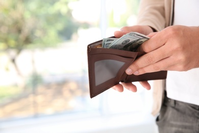 Photo of Man holding wallet with money on blurred background, closeup. Space for text