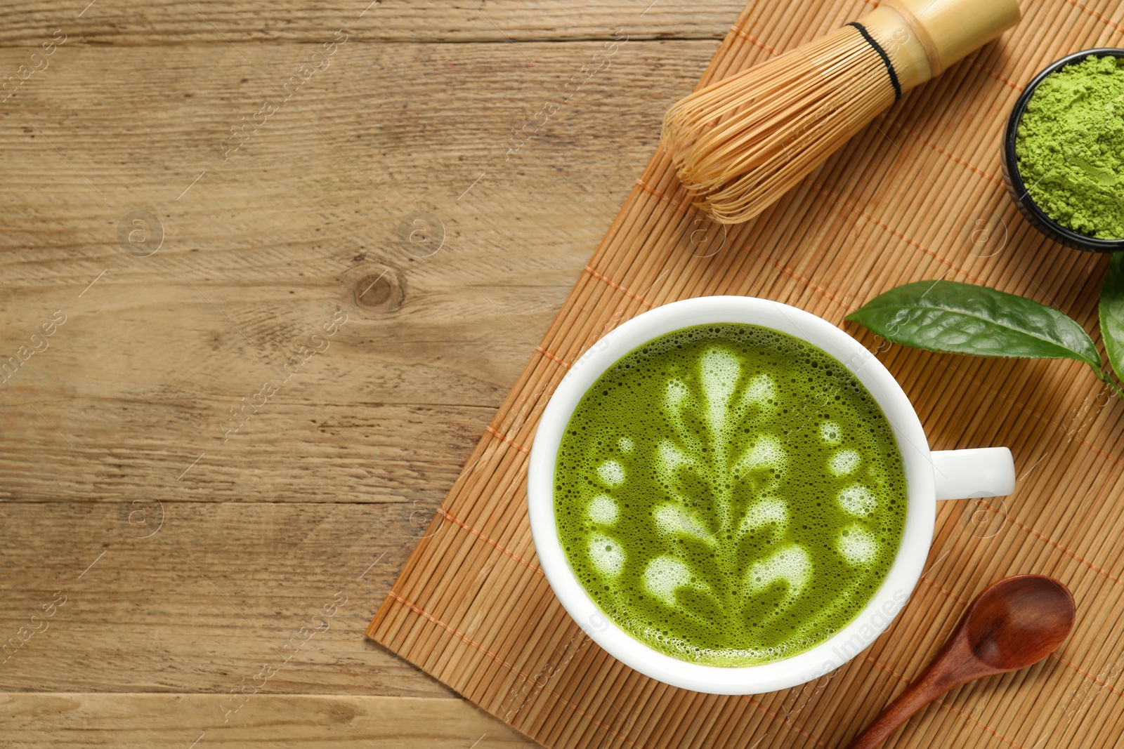 Photo of Delicious matcha latte, powder, spoon and whisk on wooden table, top view. Space for text