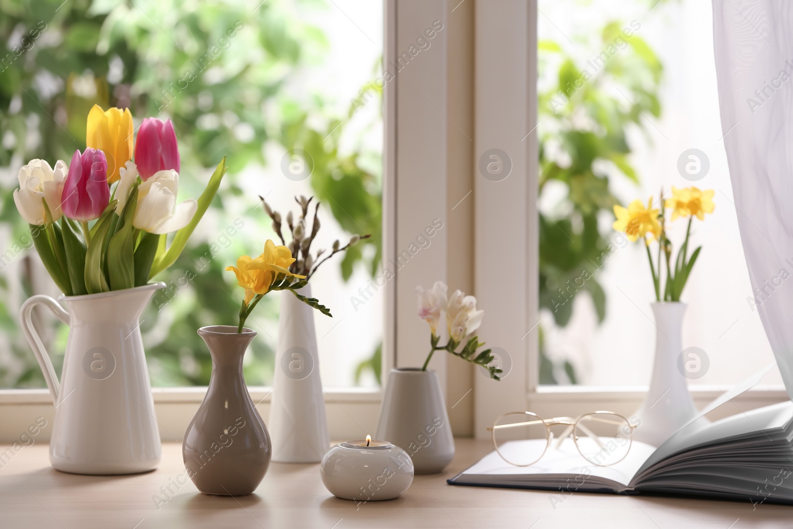Photo of Different beautiful spring flowers, burning candle and book on window sill