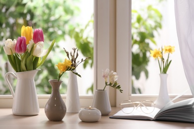 Different beautiful spring flowers, burning candle and book on window sill