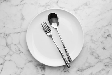Clean plate, fork and spoon on white marble table, top view
