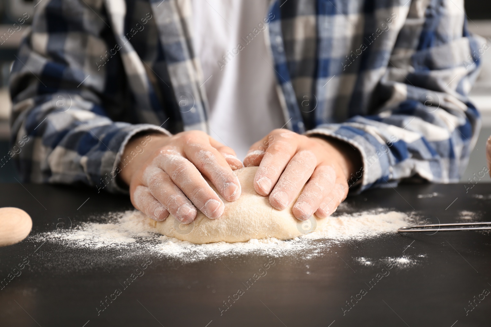 Photo of Man kneading dough on table covered with flour in kitchen