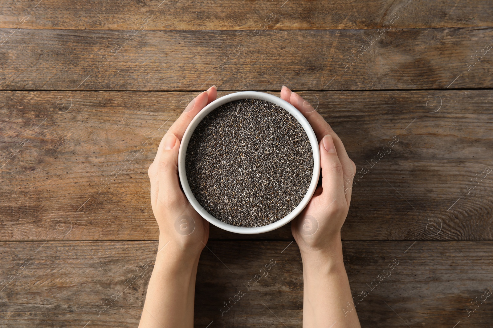 Photo of Woman holding bowl with chia seeds on wooden background, top view