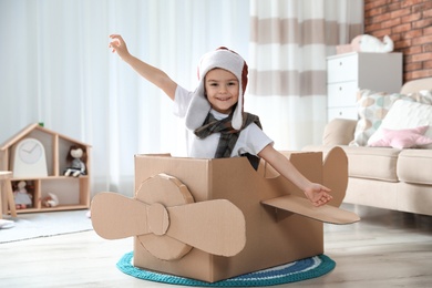 Photo of Cute little boy playing with cardboard airplane in living room