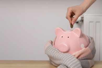 Photo of Woman putting coin into piggy bank near heating radiator, closeup. Space for text