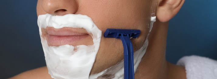Image of Man shaving with razor on blue background, closeup. Banner design
