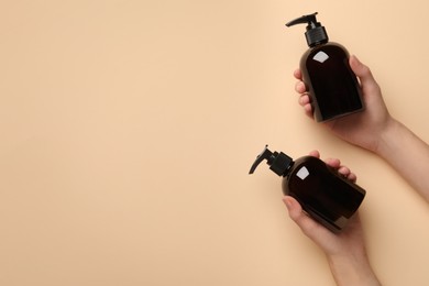 Photo of Woman holding shampoo bottles on beige background, top view. Space for text