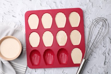 Photo of Baking mold for madeleine cookies with batter and whisk on white textured table, flat lay