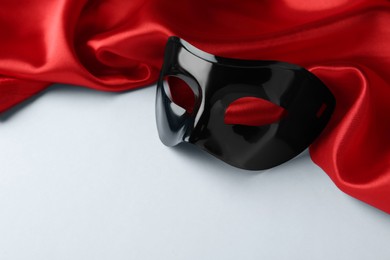 Photo of Black theatre mask and red fabric on white background, space for text