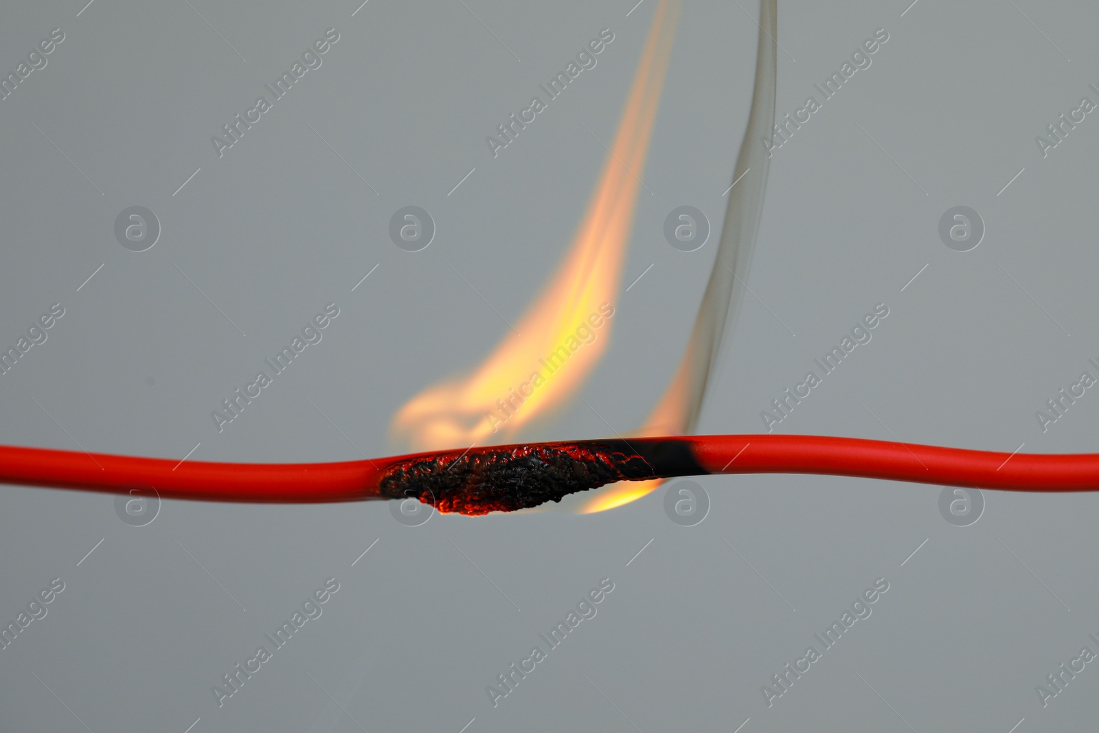 Photo of Inflamed red wire on grey background, closeup. Electrical short circuit