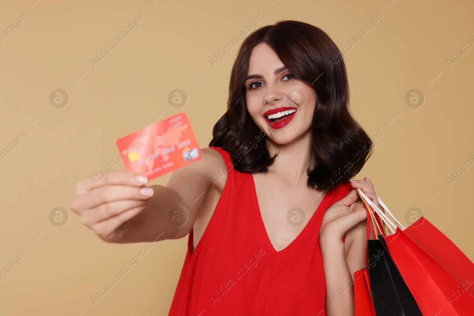 Photo of Beautiful young woman with paper shopping bags and credit card on beige background