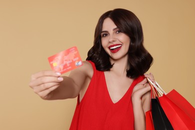 Photo of Beautiful young woman with paper shopping bags and credit card on beige background