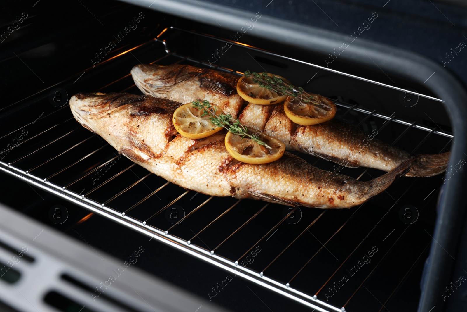 Photo of Rack with sea bass fish, lemon and thyme in oven