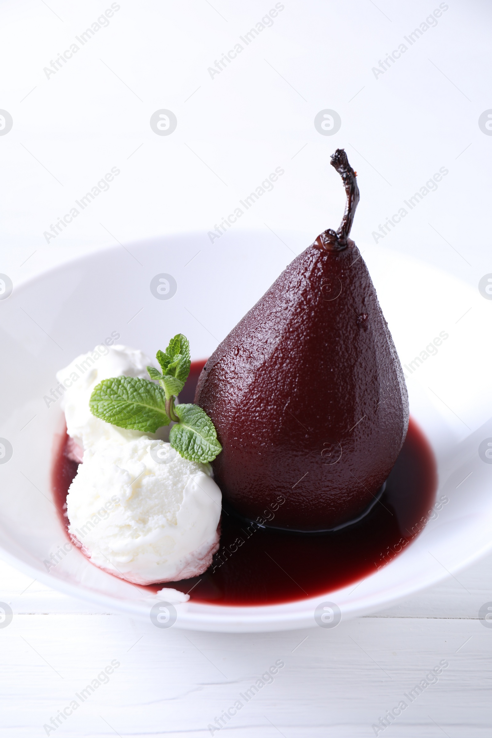 Photo of Tasty red wine poached pear with mint and Ice cream on white wooden table, closeup