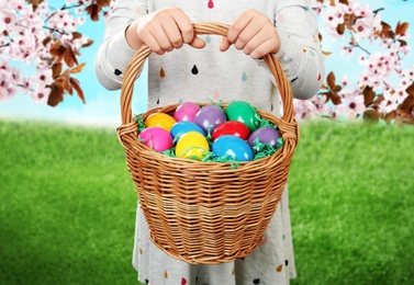 Image of Little girl with basket full of Easter eggs on green grass outdoors, closeup