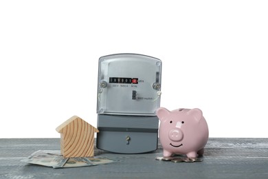 Photo of Electricity meter, house model, money and piggy bank on grey wooden table against white background