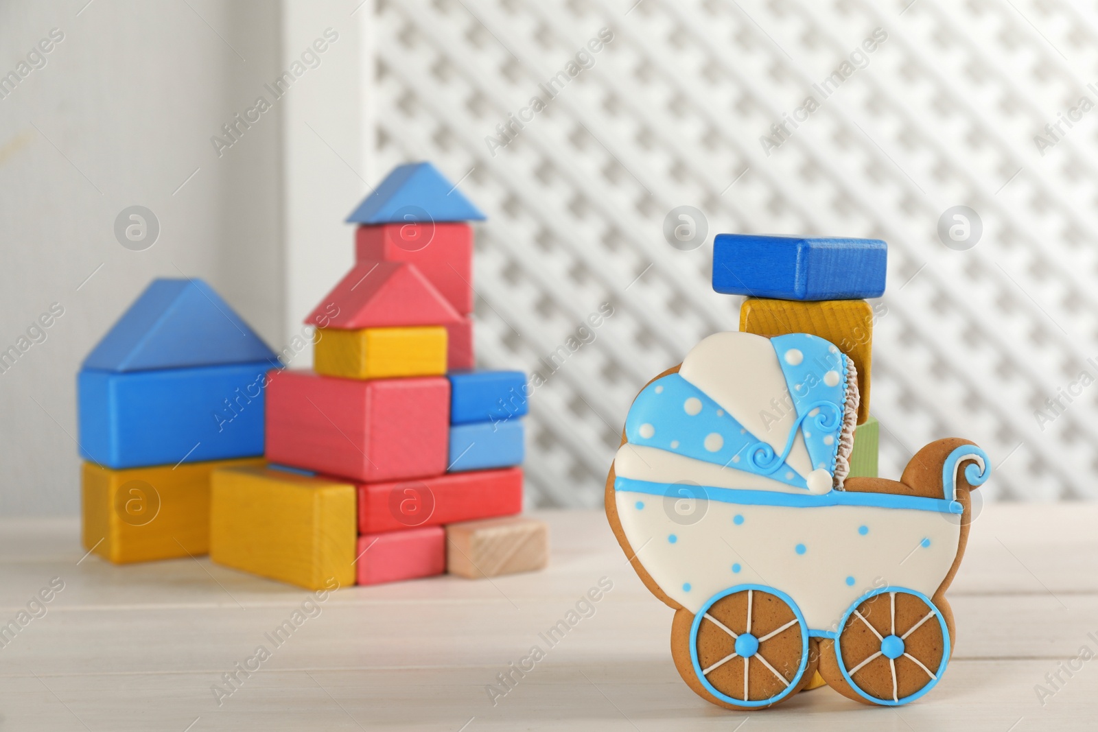 Photo of Tasty cookie in shape of stroller and colorful cubes on white wooden table, space for text. Baby shower party