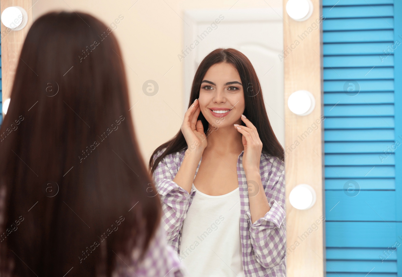 Photo of Young attractive woman looking at herself in stylish mirror at home