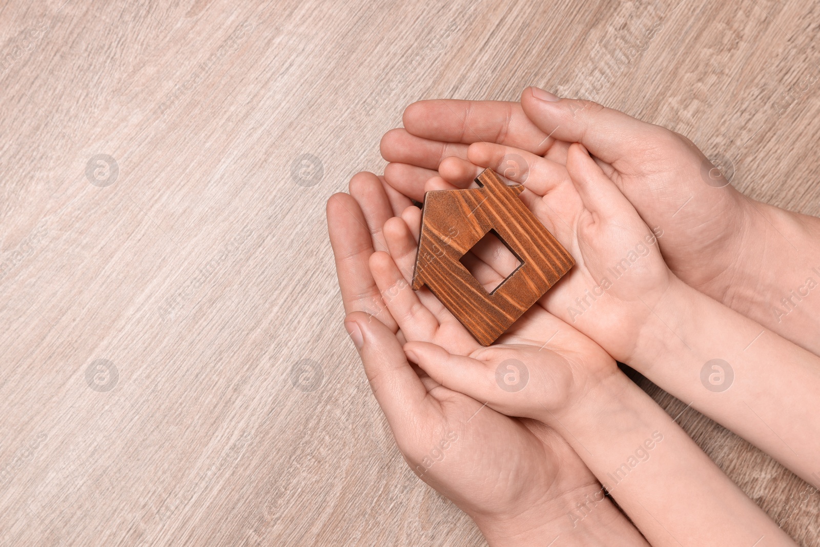 Photo of Home security concept. Man and his little child holding house model at wooden table, top view with space for text