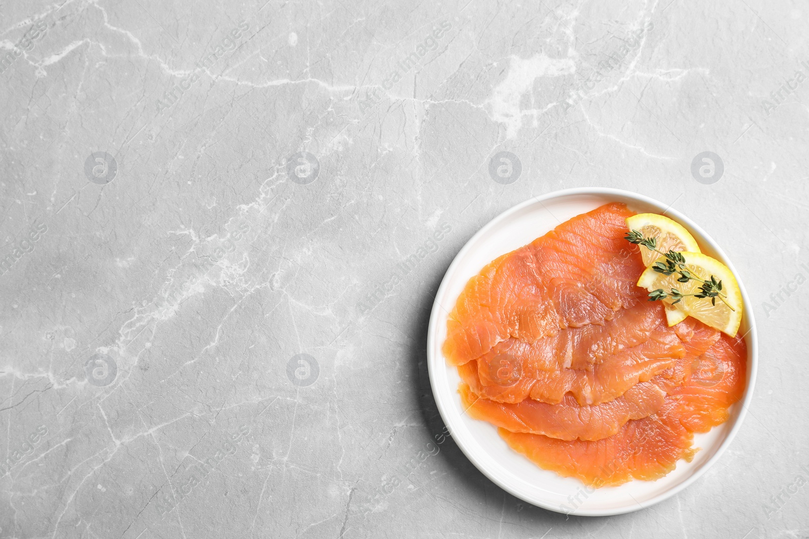 Photo of Plate with fresh sliced salmon fillet and lemon on gray background, top view