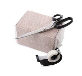 Cardboard box packed in bubble wrap, scissors and adhesive tape on white background