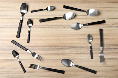 Photo of Frame made of new cutlery on wooden table, flat lay with space for text