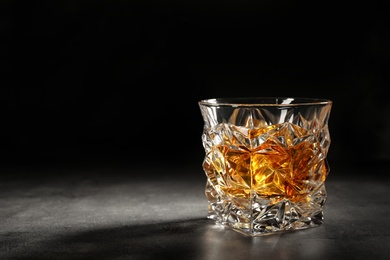 Golden whiskey in glass with ice cubes on table. Space for text