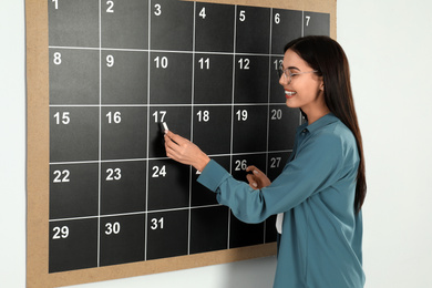 Photo of Young woman writing with chalk on board calendar