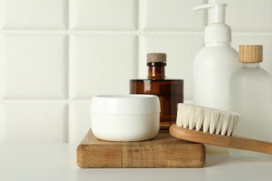 Photo of Bath accessories. Personal care products and wooden brush on white table near tiled wall, closeup