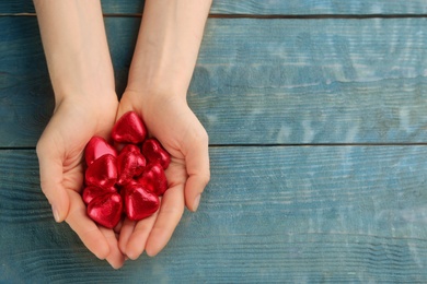 Photo of Woman holding heart shaped chocolate candies at blue wooden table, top view with space for text. Valentine's day celebration