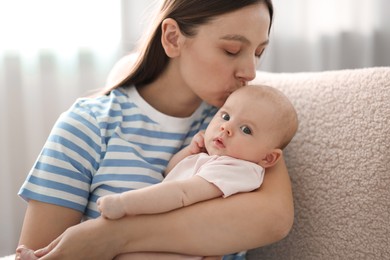Mother kissing her cute baby in armchair at home