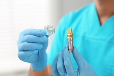 Photo of Dentist holding educational model of dental implant on blurred background, closeup