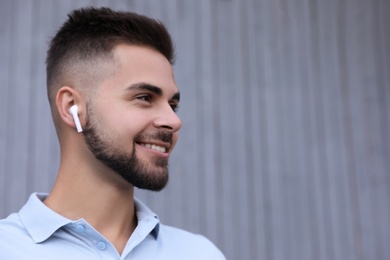 Young man with wireless headphones listening to music near grey wall. Space for text