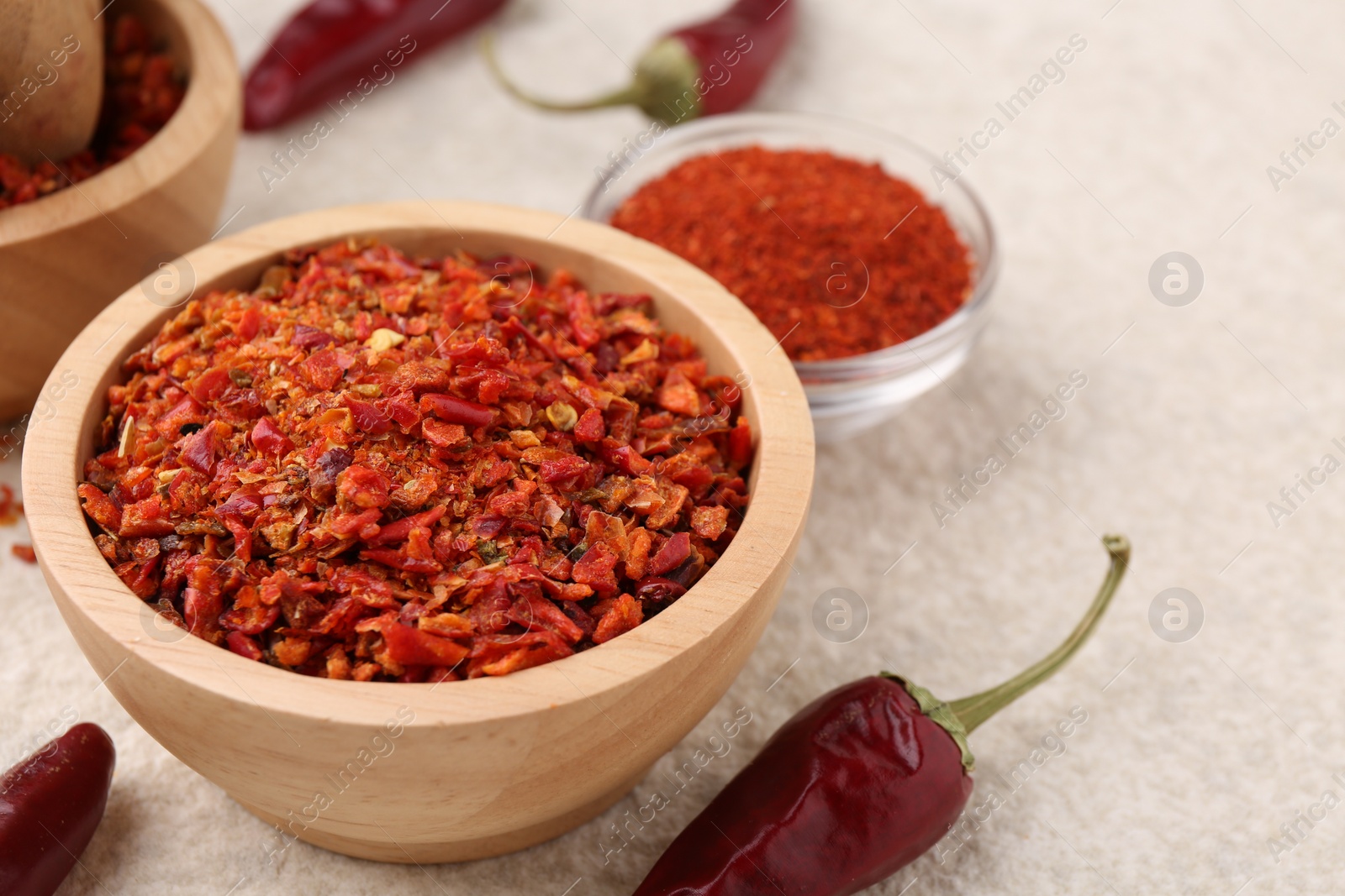 Photo of Chili pepper flakes and pods on light textured table, closeup. Space for text