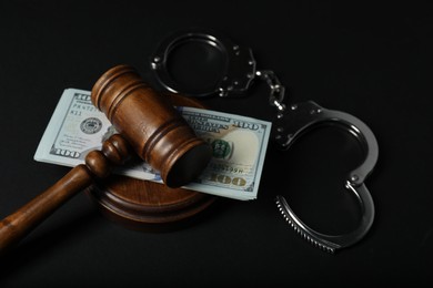 Photo of Law gavel, dollars and handcuffs on dark table