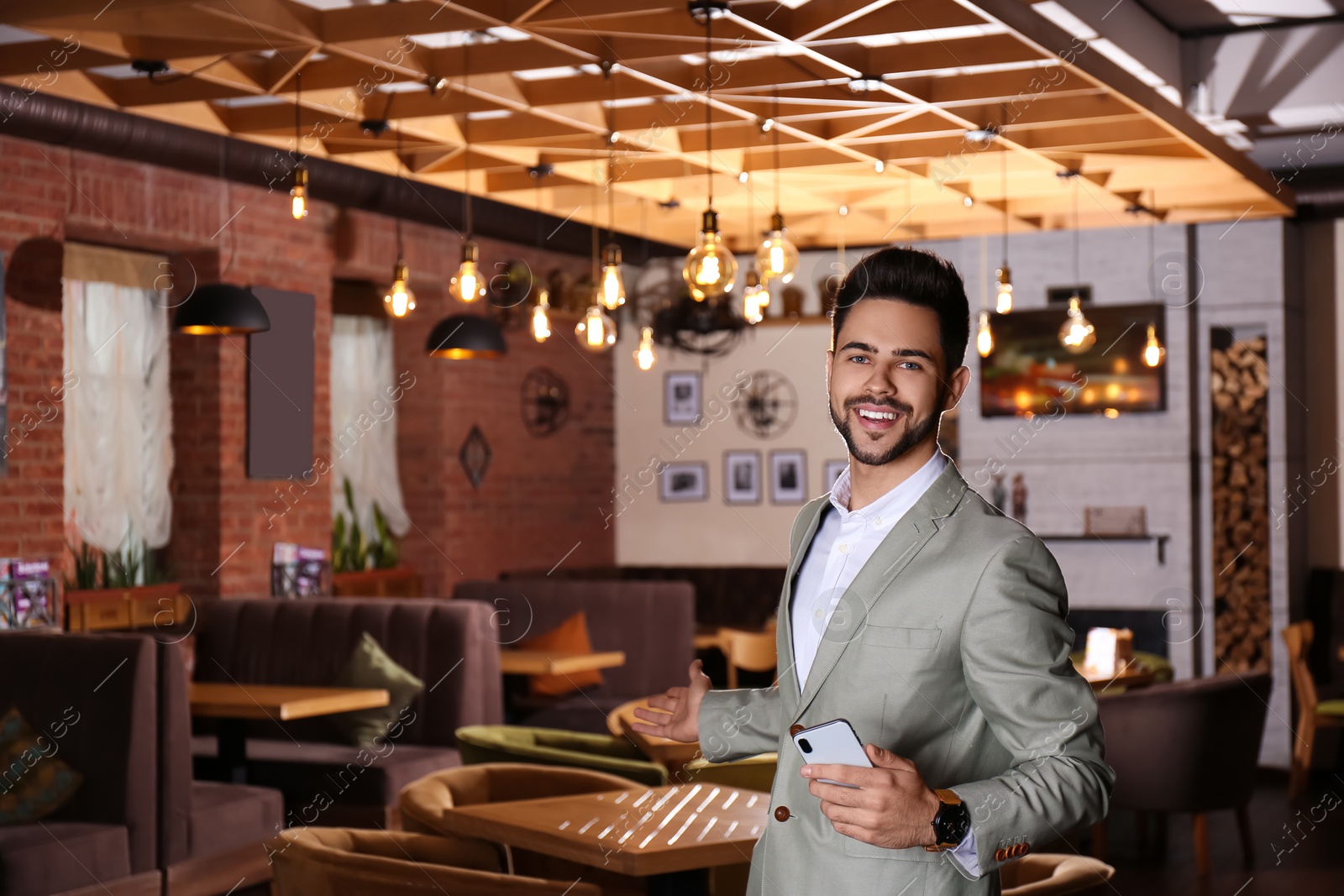 Photo of Young business owner with phone in his cafe. Space for text