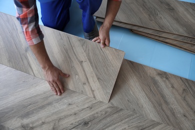 Photo of Worker installing laminated wooden floor indoors, closeup